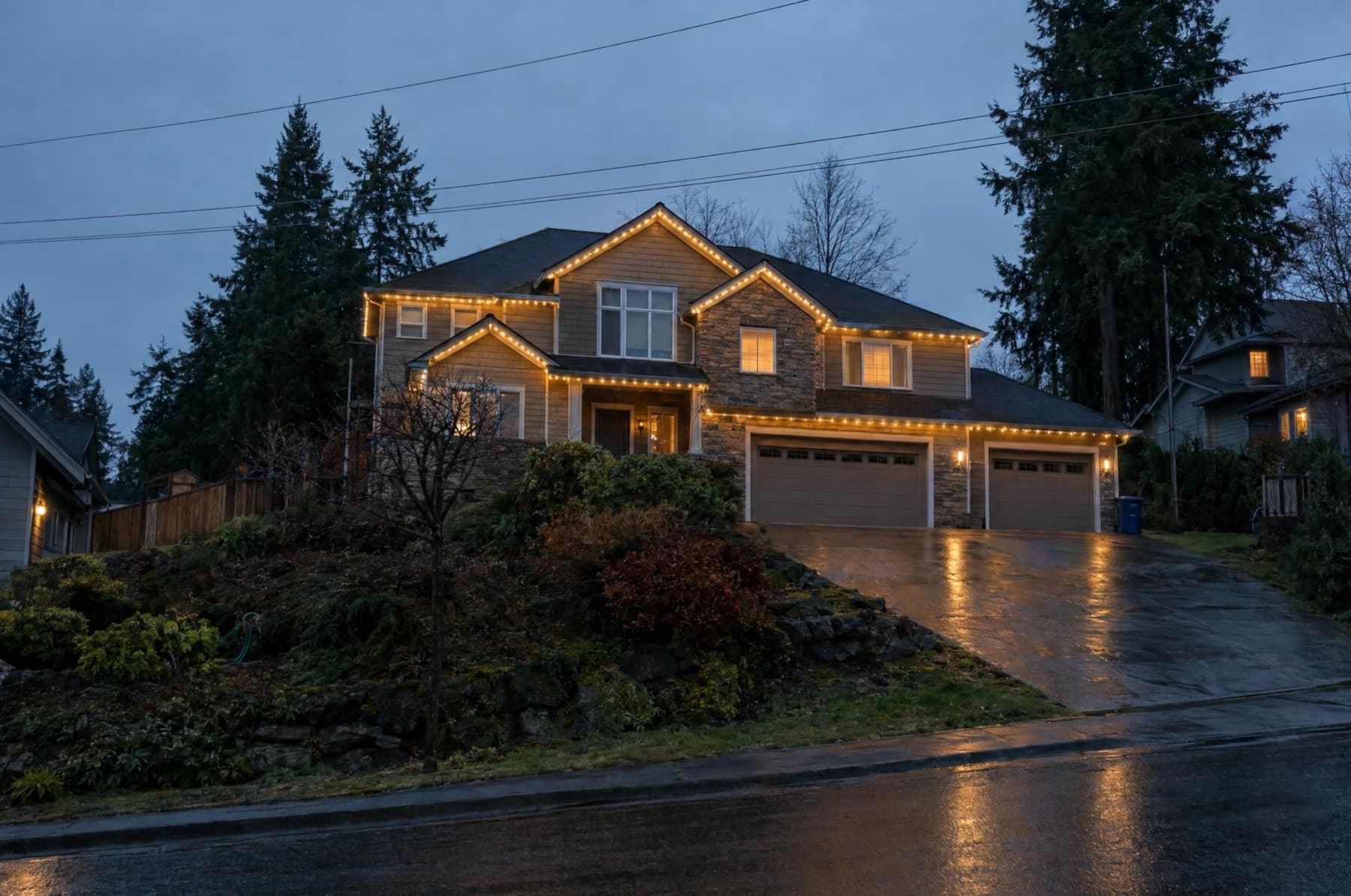 Large hillside home lit bright warm white, seen from the road below