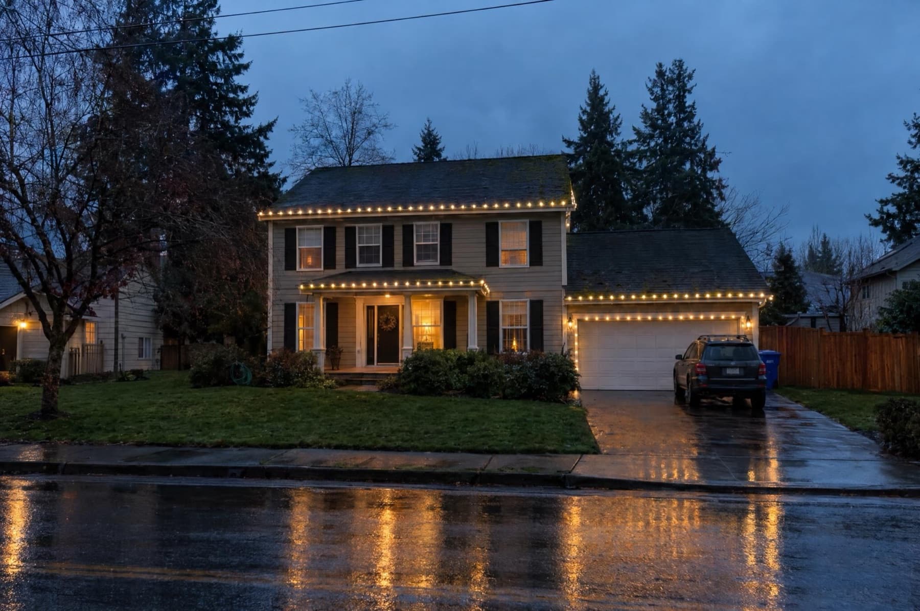Colonial-style home with warm-white C9 strands clipped along the rooflines in light rain